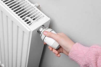 Photo of Girl adjusting heating radiator thermostat near white wall indoors, closeup