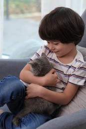 Photo of Cute little boy with kitten in armchair at home. Childhood pet