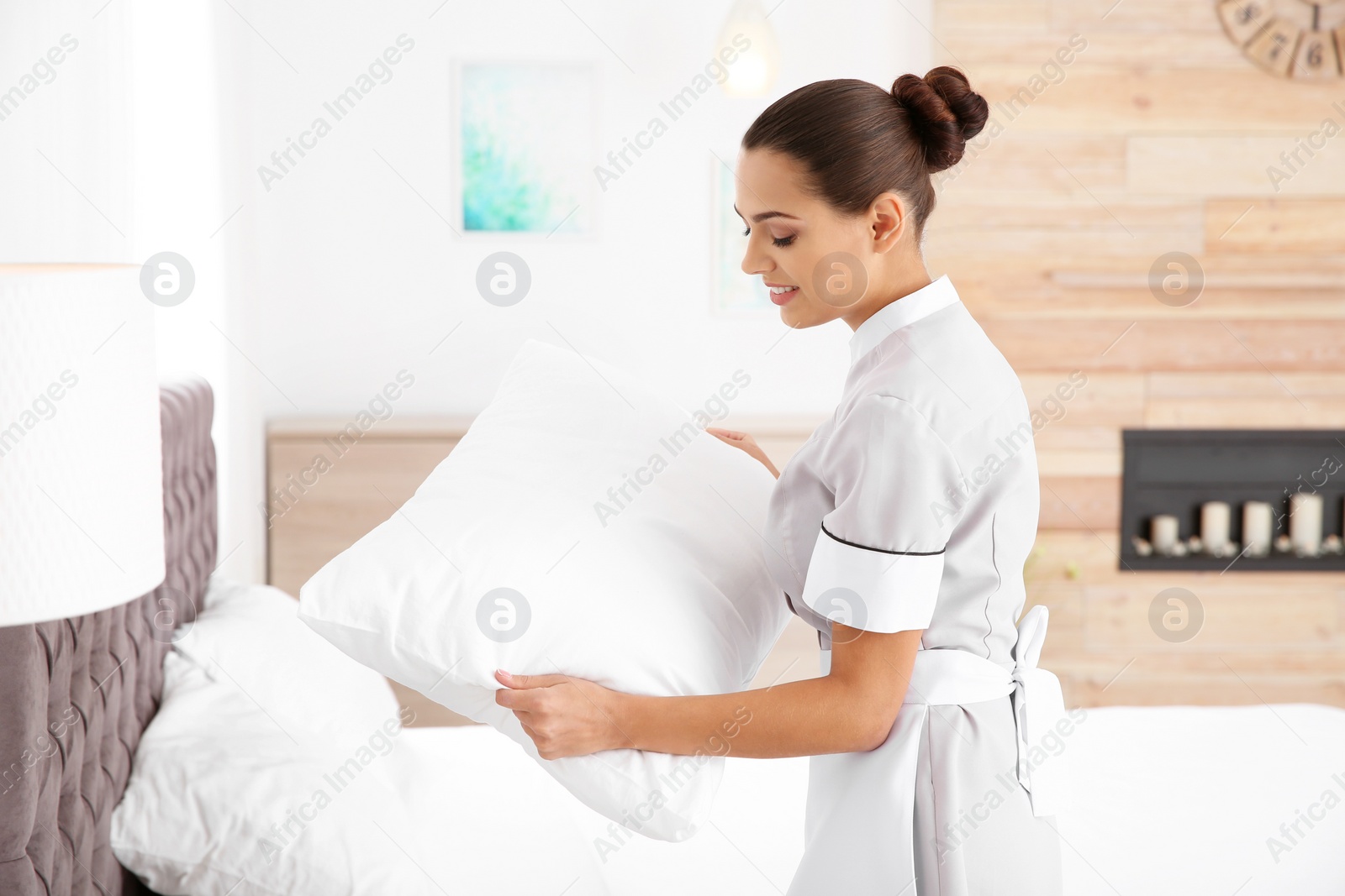 Photo of Young chambermaid making bed in hotel room