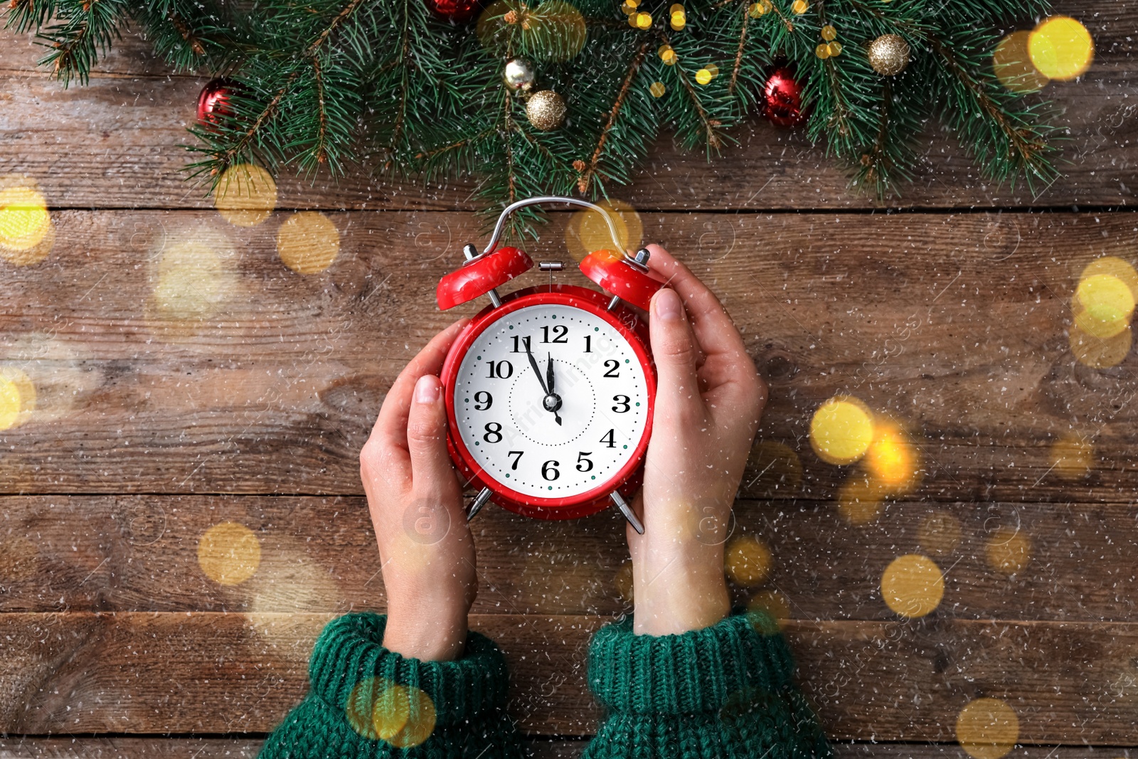 Image of Woman holding alarm clock near Christmas decor over wooden background, top view. New Year countdown