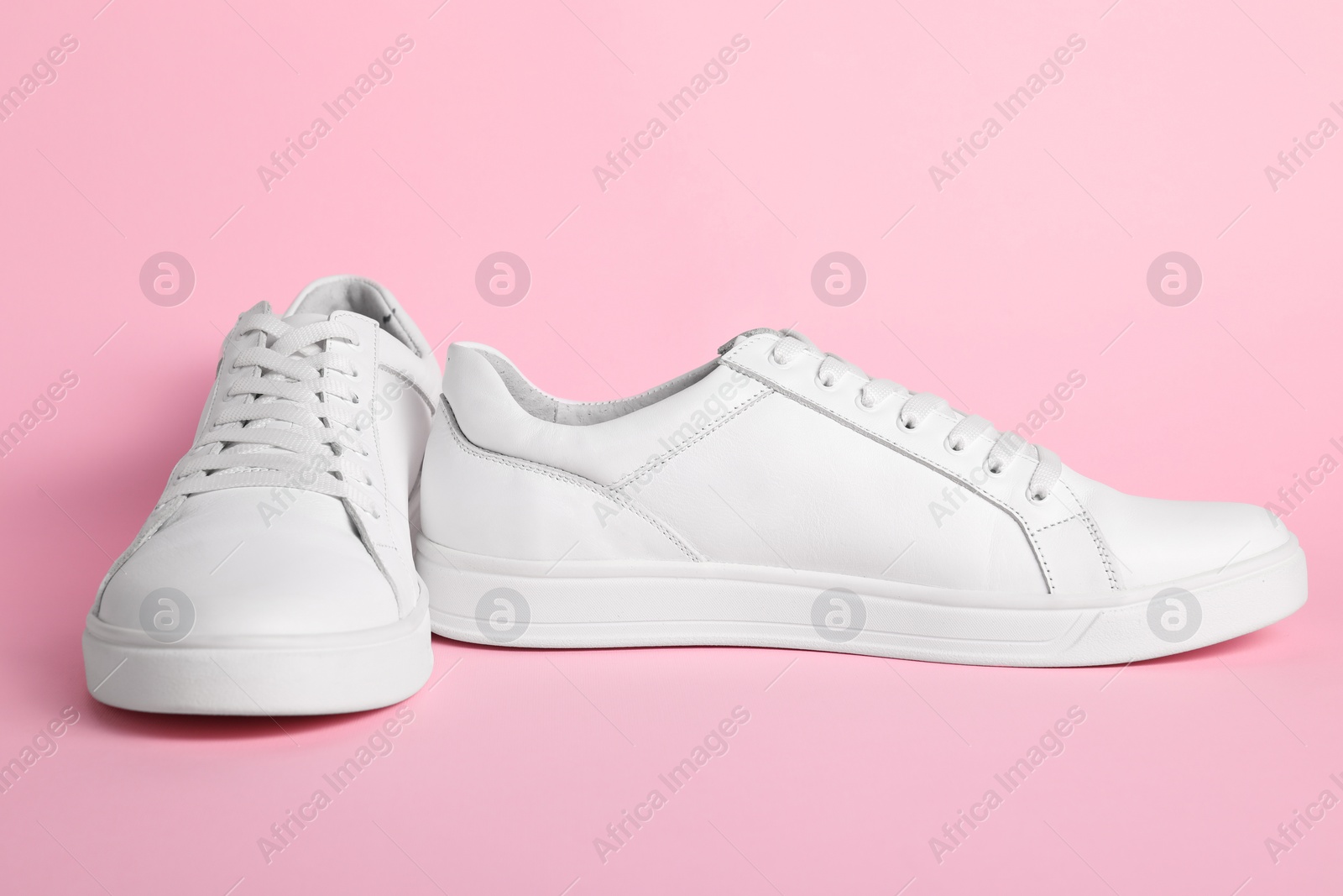 Photo of Pair of stylish white sneakers on pink background