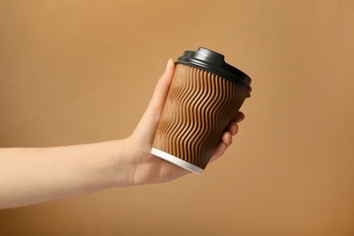 Photo of Woman holding takeaway paper coffee cup on brown background, closeup
