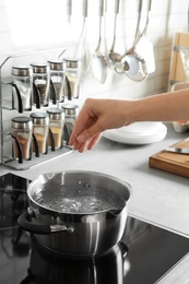 Woman salting boiling water in pot on stove, closeup