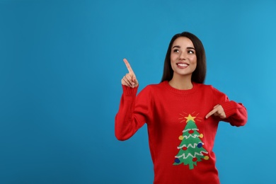 Young woman in Christmas sweater on blue background, space for text