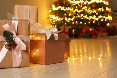 Photo of Beautiful gift boxes against fir tree with Christmas lights indoors, space for text