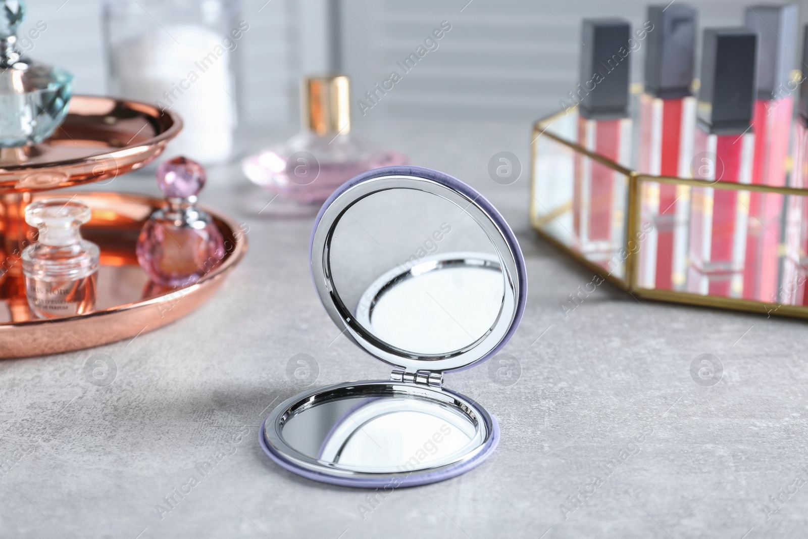 Photo of Stylish pocket mirror and cosmetic products on grey table