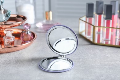 Stylish pocket mirror and cosmetic products on grey table