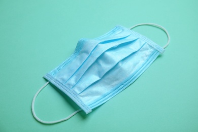 Photo of Medical face mask on turquoise background, closeup