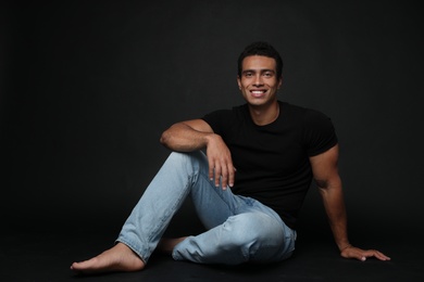 Handsome young African-American man sitting on black background