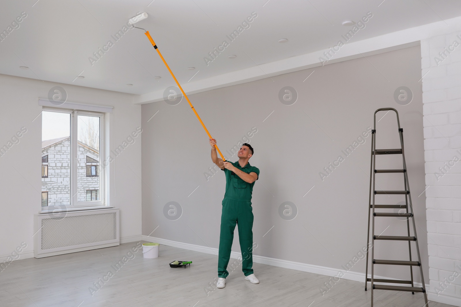 Photo of Man painting ceiling with roller in room