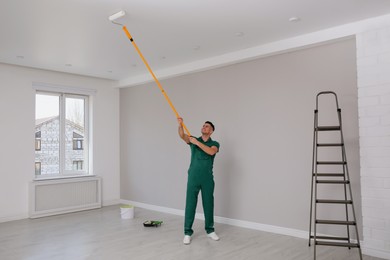 Photo of Man painting ceiling with roller in room