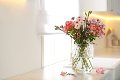 Vase with beautiful flowers on kitchen counter, space for text. Stylish element of interior design