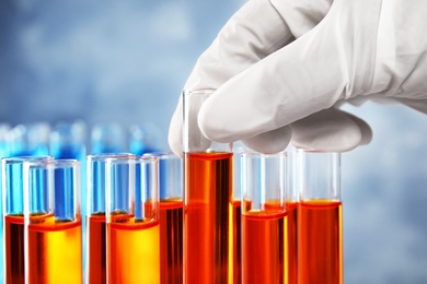 Scientist taking test tube with liquid sample on grey background, closeup