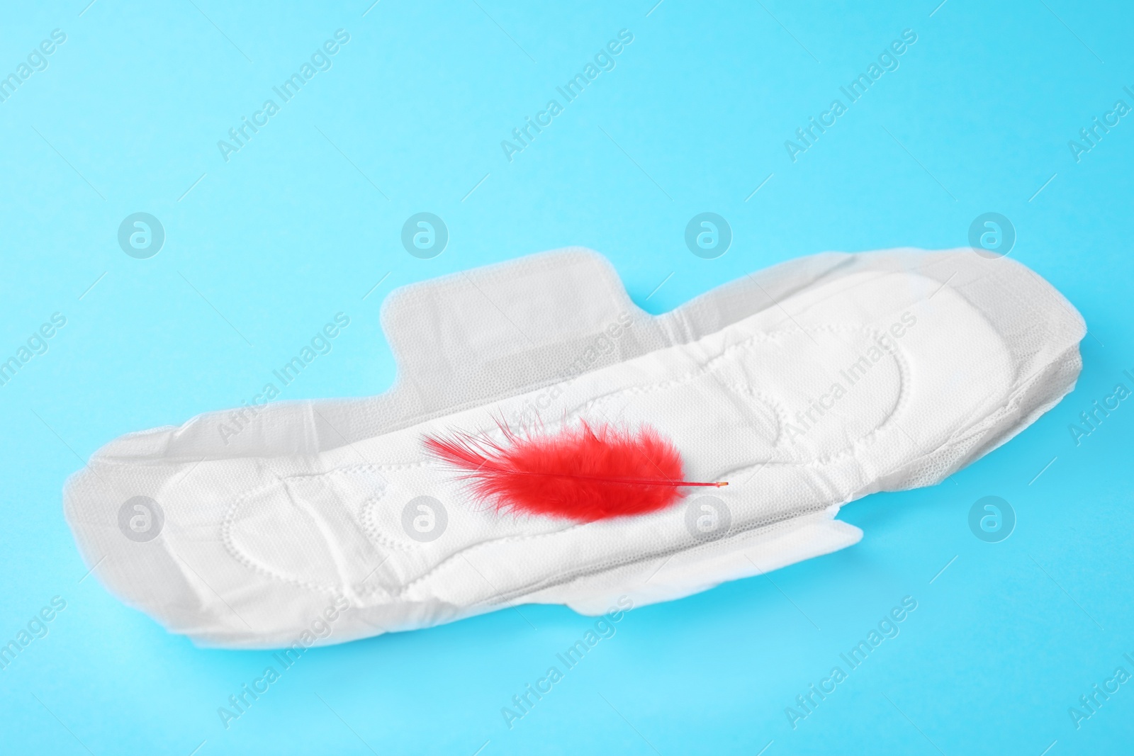 Photo of Menstrual pad and red feather on color background. Gynecological care