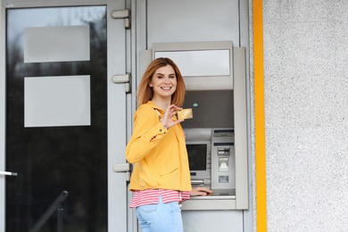 Photo of Beautiful woman with credit card near  cash machine outdoors. Space for text