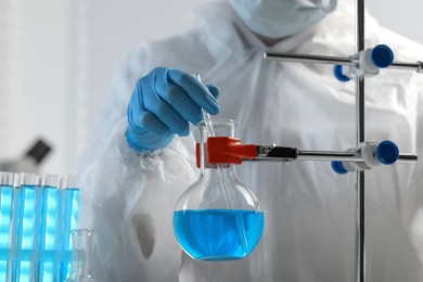 Scientist taking sample of light blue liquid in laboratory, closeup