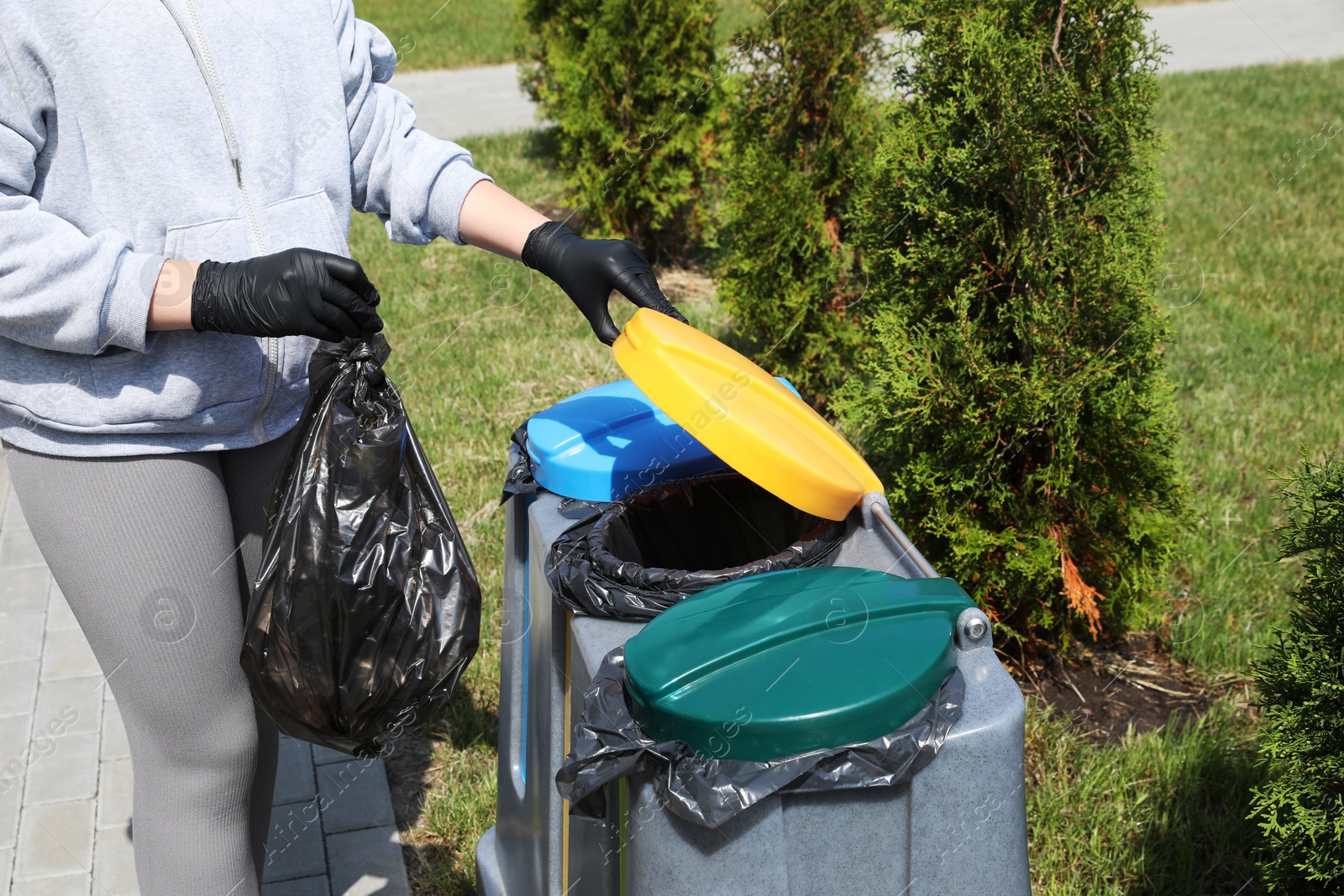 Photo of Woman throwing trash bag full of garbage in bin outdoors, closeup. Recycling concept