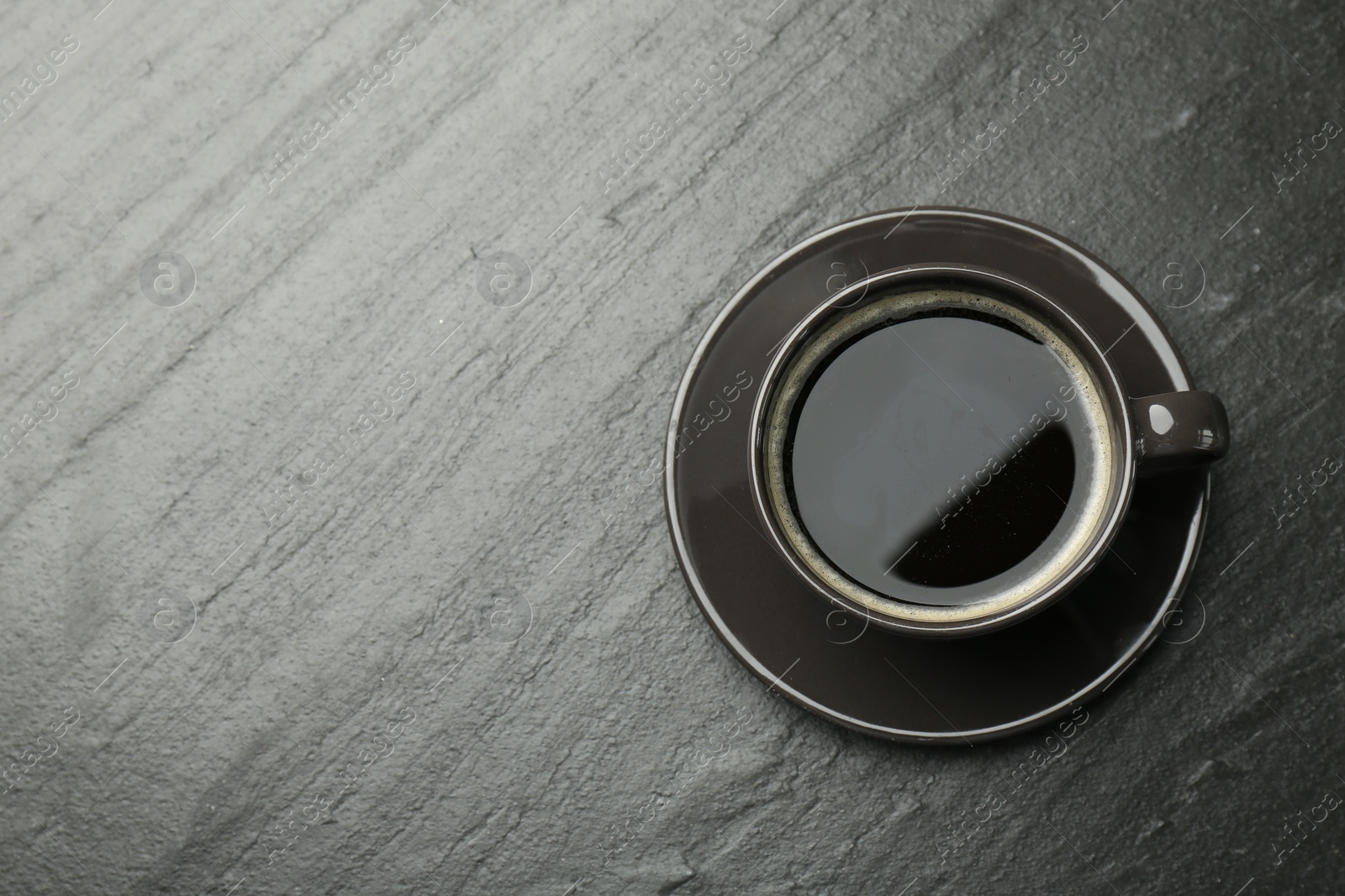 Photo of Hot coffee in cup on dark textured table, top view. Space for text
