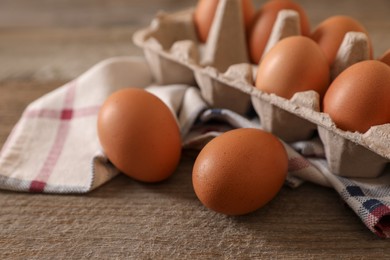 Raw chicken eggs with carton and cloth napkin on wooden table, closeup
