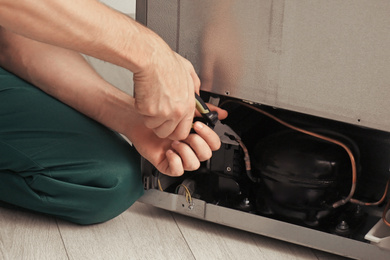 Image of Electrician with pliers fixing refrigerator indoors, closeup 