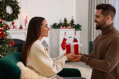 Beautiful young couple with Christmas gift at home