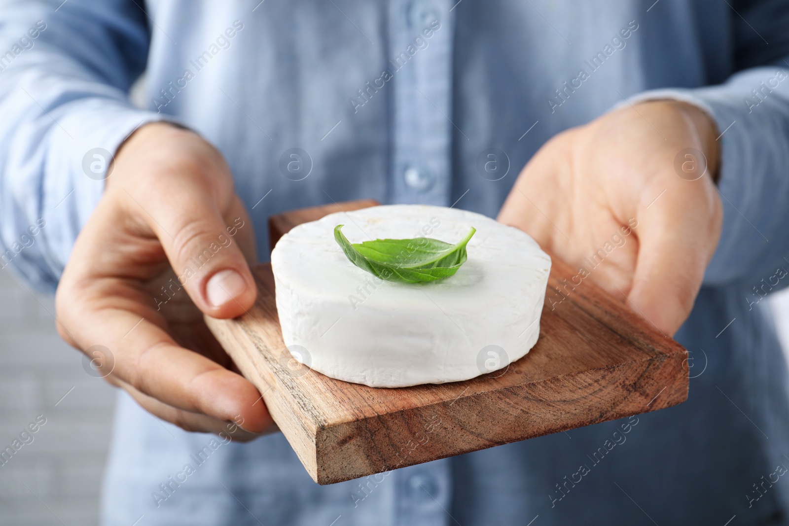 Photo of Woman holding serving board with delicious brie cheese on blurred background, closeup