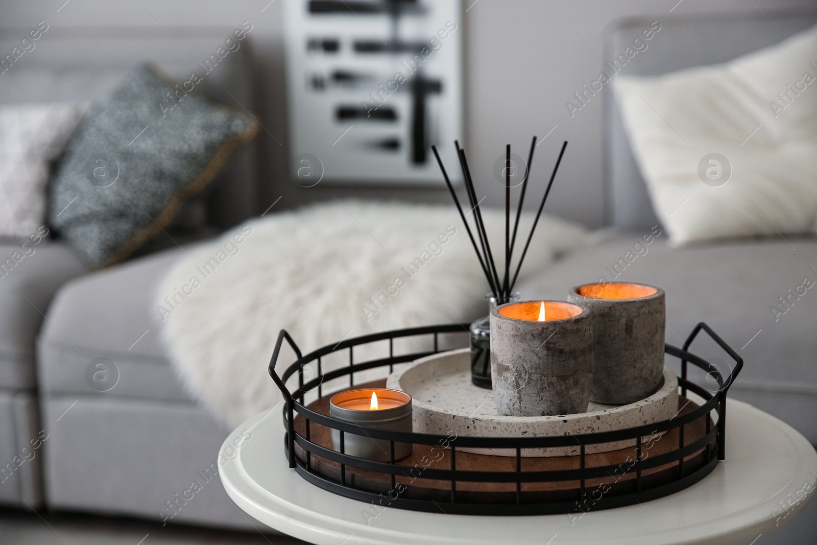 Photo of Candles and aroma reed diffuser on white table near grey sofa