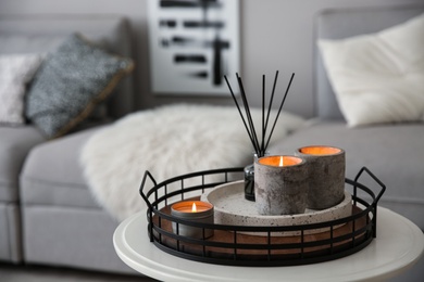 Candles and aroma reed diffuser on white table near grey sofa