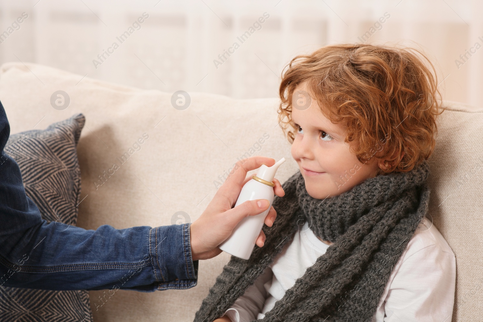 Photo of Mother using nasal spray to treat her little son on sofa indoors, closeup