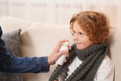 Mother using nasal spray to treat her little son on sofa indoors, closeup