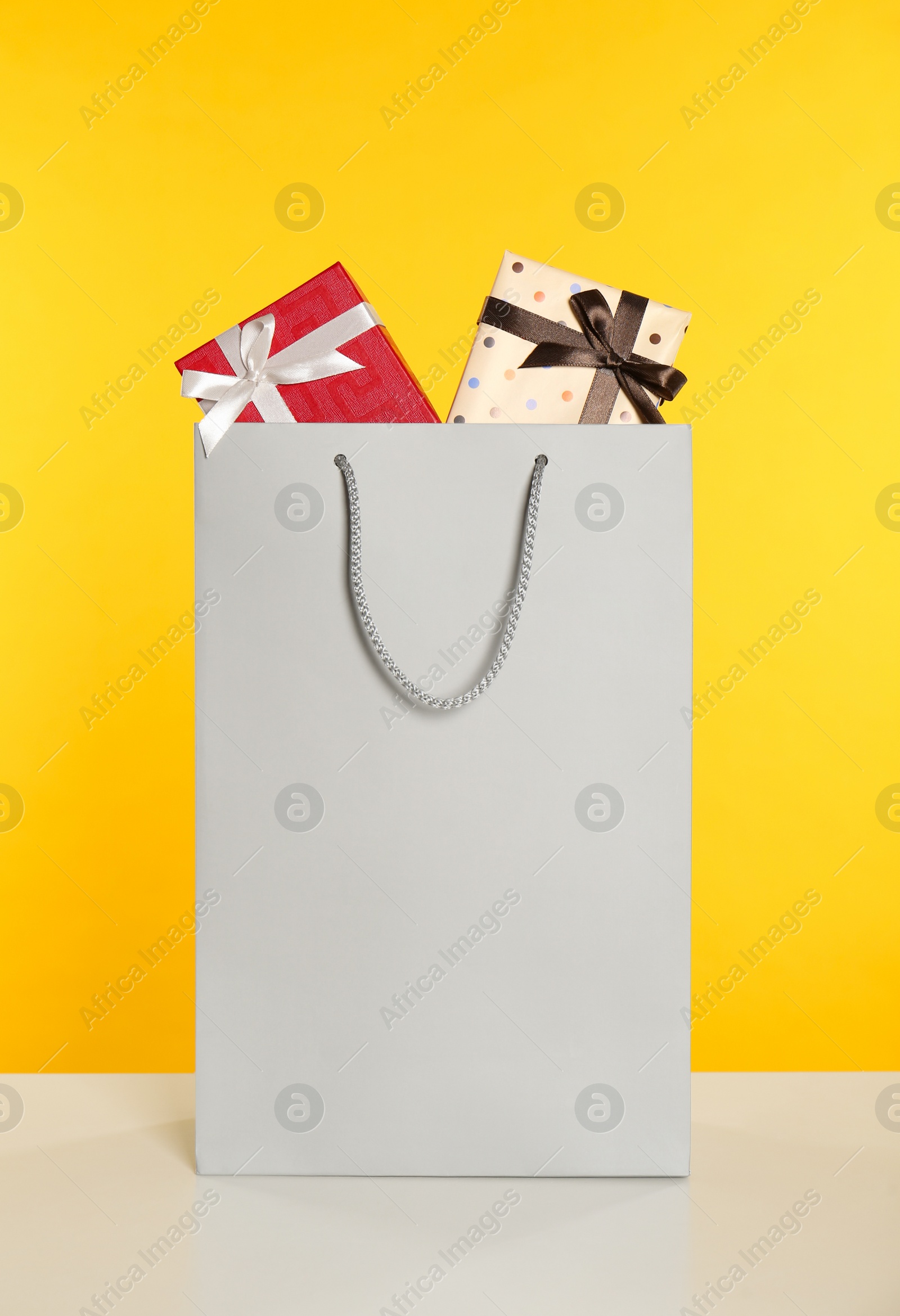 Photo of Paper shopping bag full of gift boxes on yellow background