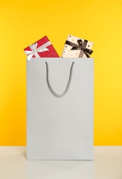 Photo of Paper shopping bag full of gift boxes on yellow background