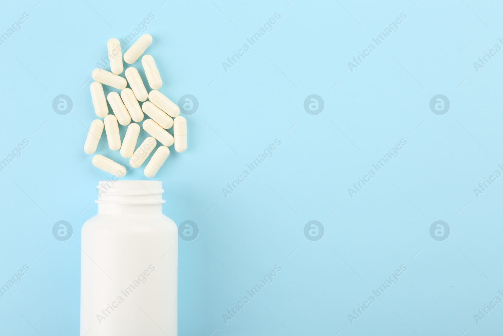 Photo of Bottle and vitamin capsules on light blue background, top view. Space for text