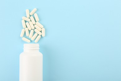 Photo of Bottle and vitamin capsules on light blue background, top view. Space for text