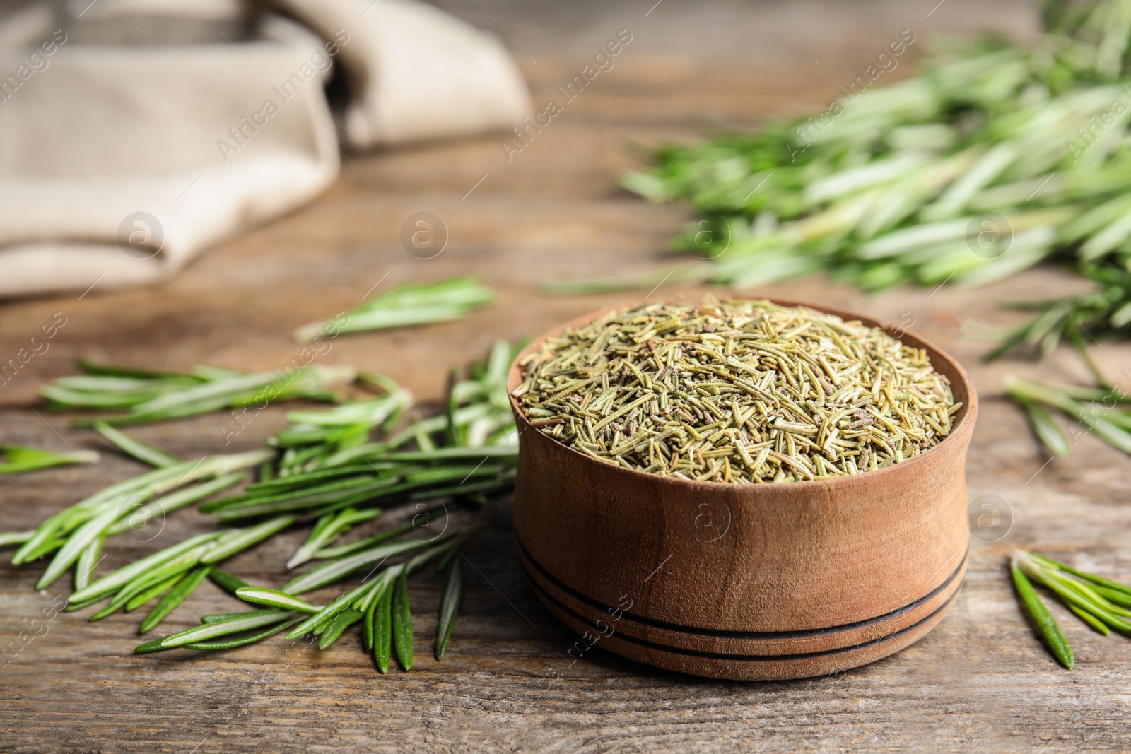 Photo of Bowl of dried rosemary and fresh leaves on wooden table, space for text