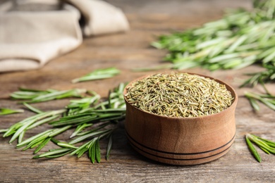 Bowl of dried rosemary and fresh leaves on wooden table, space for text