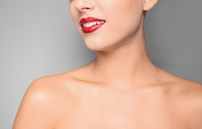 Photo of Beautiful young woman with red glossy lips on gray background, closeup