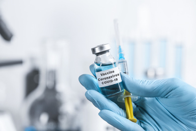 Doctor holding coronavirus vaccine and syringe in laboratory, closeup