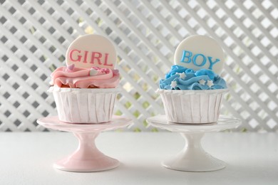 Photo of Delicious cupcakes decorated with Girl and Boy toppers for baby shower on white table