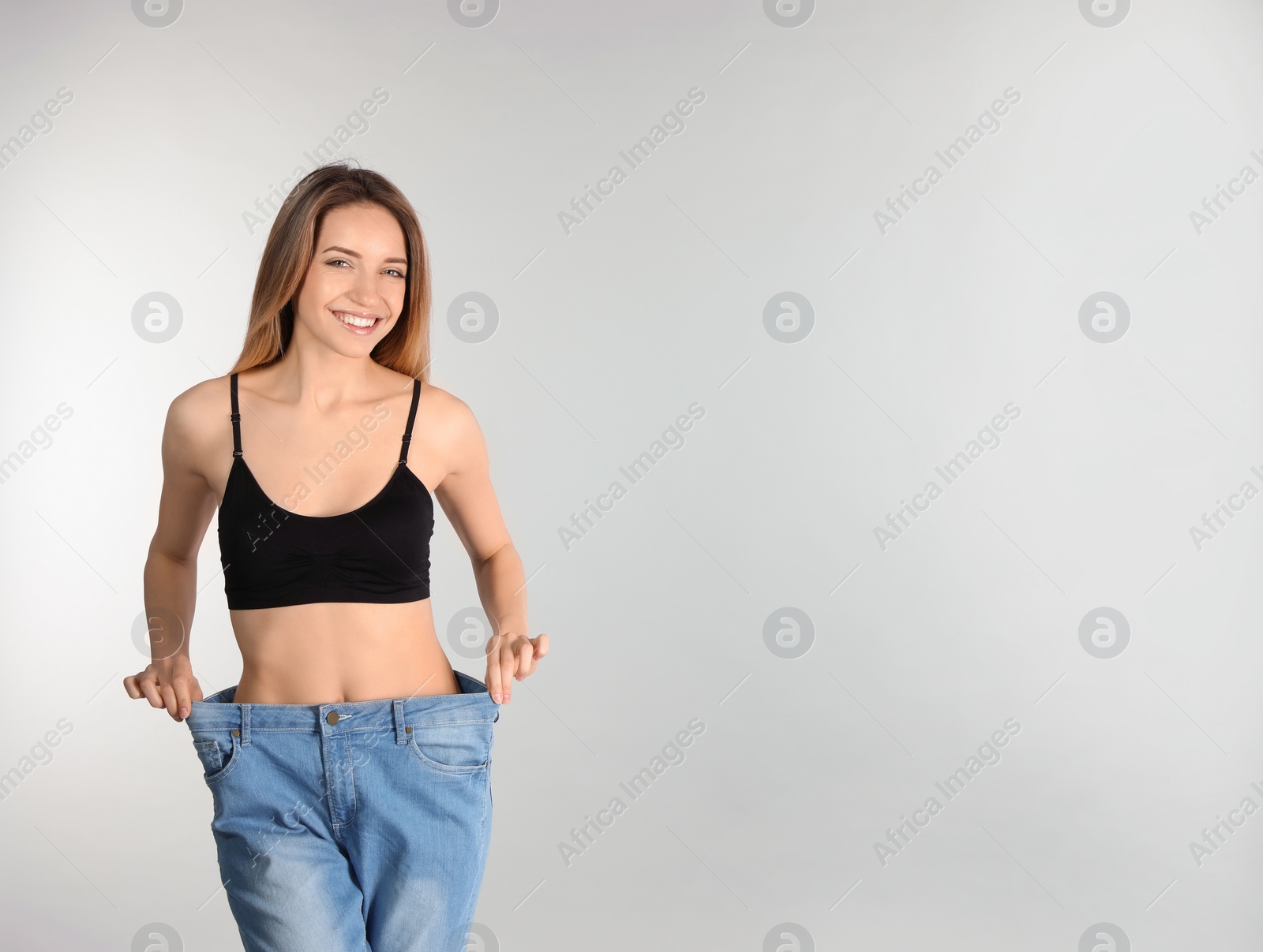 Photo of Slim woman in oversized jeans on light background, space for text. Perfect body