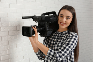 Photo of Operator with professional video camera near white brick wall