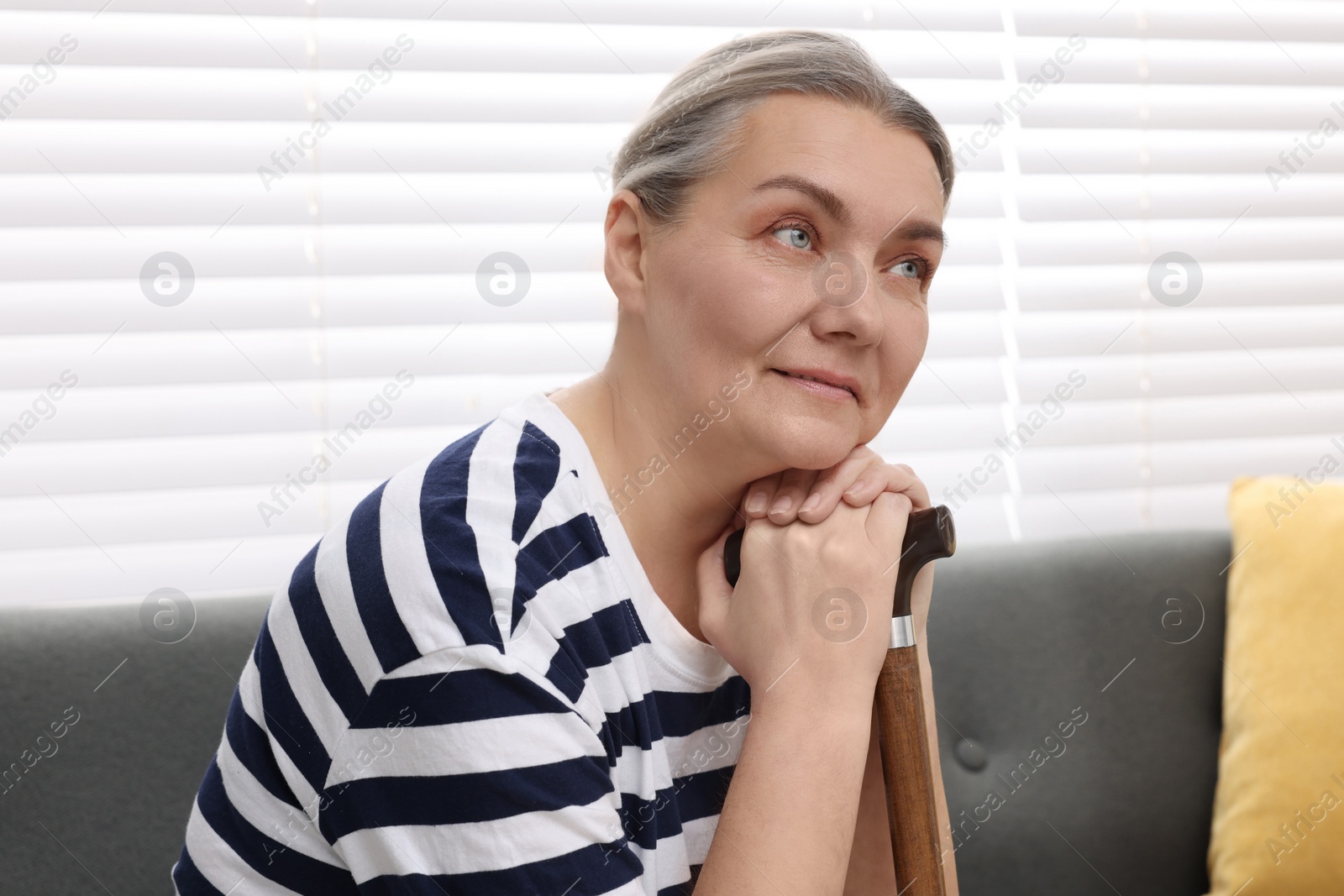 Photo of Senior woman with walking cane sitting on sofa at home