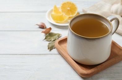Photo of Hot delicious bouillon in cup on white wooden table. Space for text