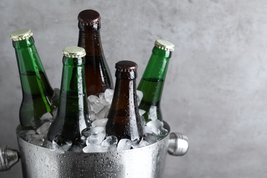 Metal bucket with bottles of beer and ice cubes on grey background, closeup