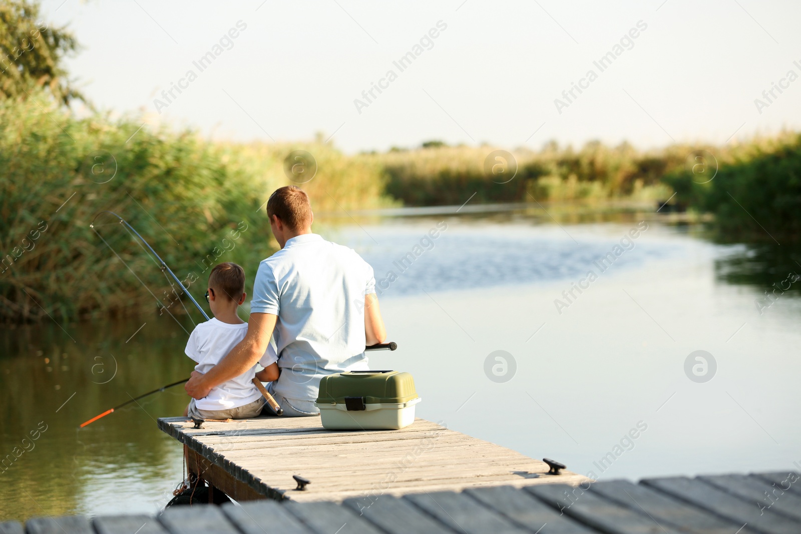 Photo of Dad and son fishing together on sunny day. Space for text