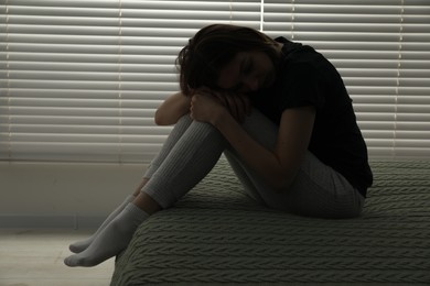 Sad young woman sitting on bed at home