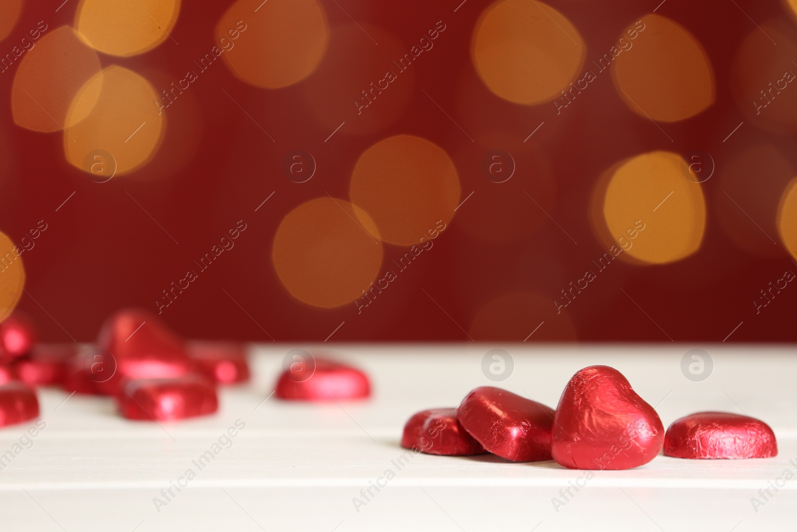 Photo of Heart shaped chocolate candies on white table against blurred lights, space for text. Valentines's day celebration