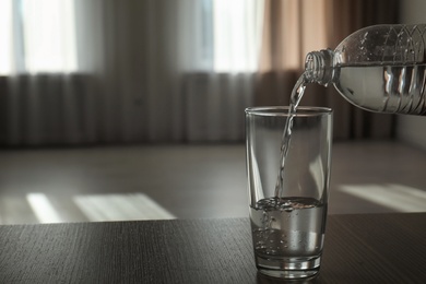 Photo of Pouring water from bottle into glass on blurred background. Space for text