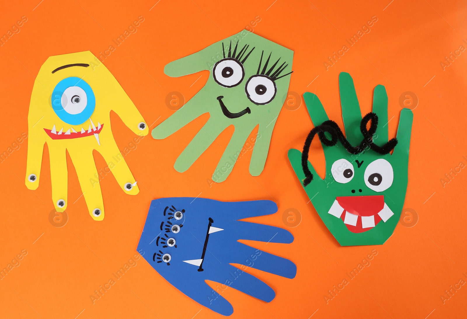 Photo of Funny hand shaped monsters on orange background, flat lay. Halloween decoration