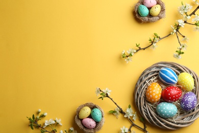 Photo of Flat lay composition with painted Easter eggs and blossoming branches on color background, space for text